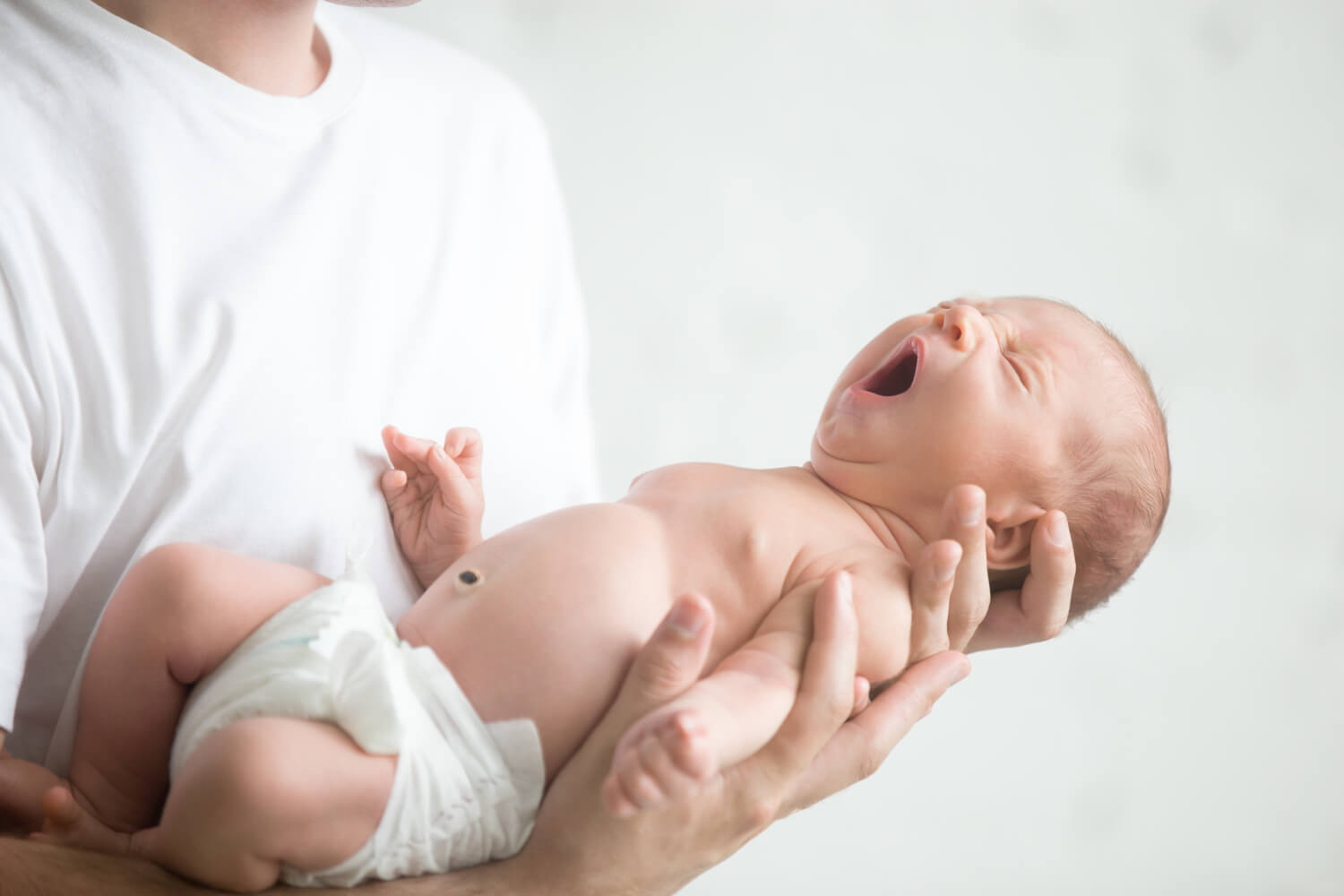 Папа держит плачущего новорожденного на руках